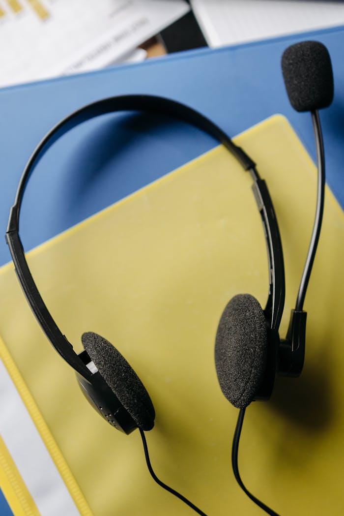 Close-up of a black headset resting on a yellow folder on a blue surface.