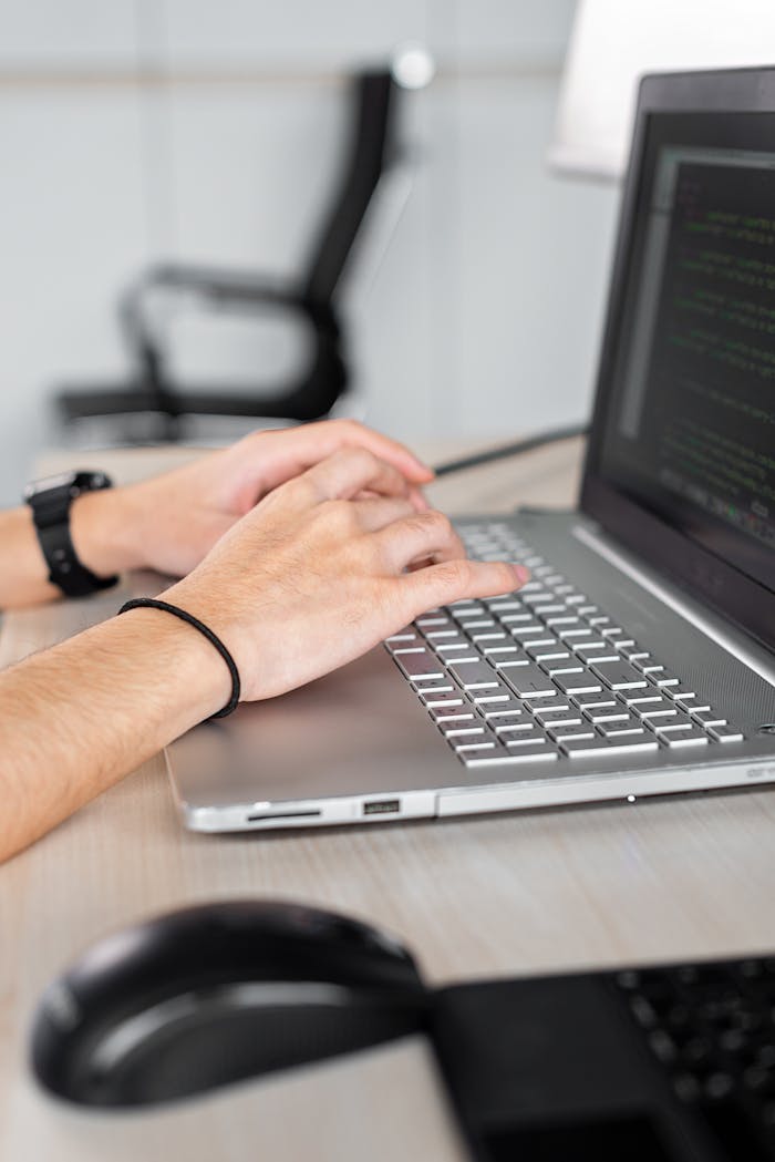 Person typing on a laptop, focusing on hands and code on screen in a modern office.